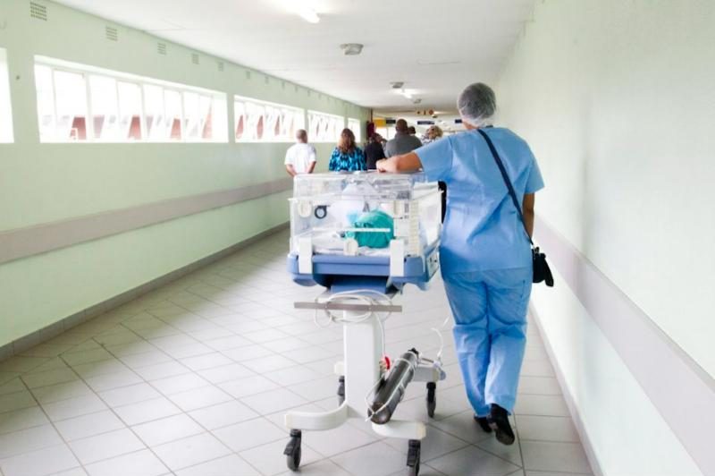 Νοσηλεύτρια με ιατρική στολή σπρώχνει θερμοκοιτίδα σε διάδρομο νοσοκομείου