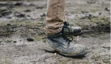 Λερωμένα δερμάτινα μποτάκια εργασίας σε χωμάτινο εργοτάξιο